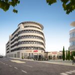 Modernes Gebäude mit runder Fassade, Geschäften im Erdgeschoss und klar blauem Himmel.