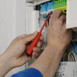 Eine Person arbeitet an einem elektrischen Verteiler mit einem roten Schraubendreher.