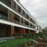 Moderne Wohnanlage mit Holzelementen, Balkonen und grünem Garten im Vordergrund. Bewölkter Himmel.