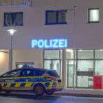 Ein Polizeiwagen steht vor einem modernen Polizeigebäude mit leuchtendem Schild.
