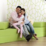 Eine Familie sitzt auf einer grünen Couch und umarmt sich in einem freundlichen Raum.